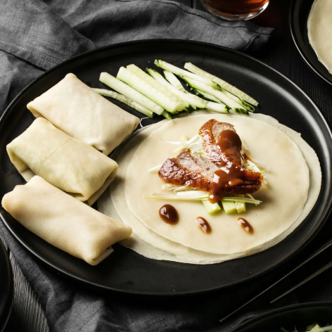 Plated dish with pancakes, braised meat, and vegetables on a dark surface